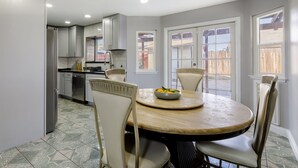 A modern kitchen with white cabinets, a dining table with chairs, and a window with a view of a wooden fence. - Modern 3BR Bay Stay: pet/family-friendly, yard, parking, W/D, near hospitals (MORENO VALLEY)