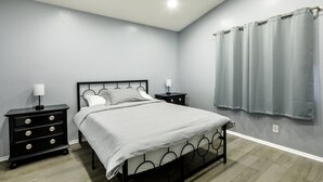 A bedroom with a bed, two bedside tables, a nightstand, a window with curtains, and a light switch on the wall. - Modern 3BR Bay Stay: pet/family-friendly, yard, parking, W/D, near hospitals (MORENO VALLEY)