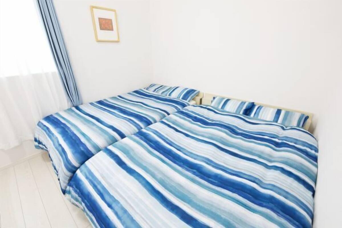 A double bed with striped bedding, a framed picture on the wall, and a window with curtains.