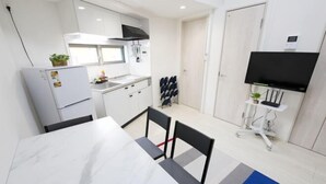 A compact kitchen with white cabinets, a built-in oven, and a flat-screen TV mounted on the wall. - Nishi-Shinjuku-Villa (Tokyo)
