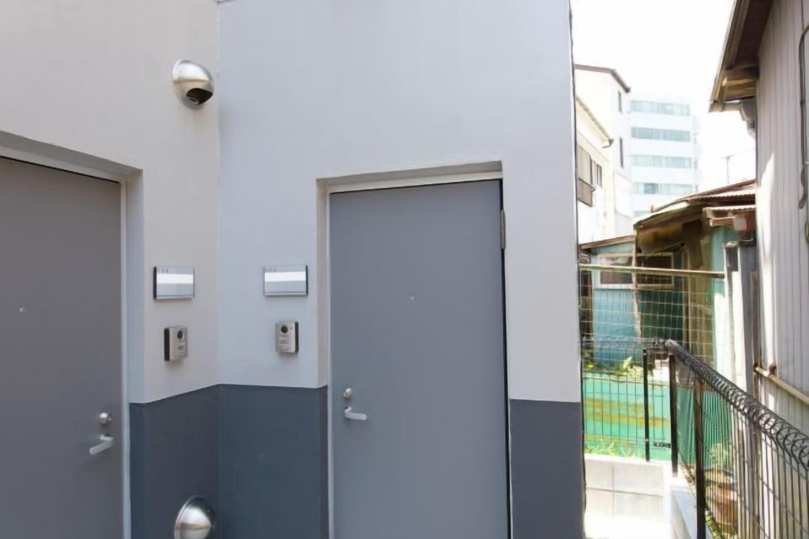 A building exterior with two doors, a security camera, and a fenced area with a building in the background.