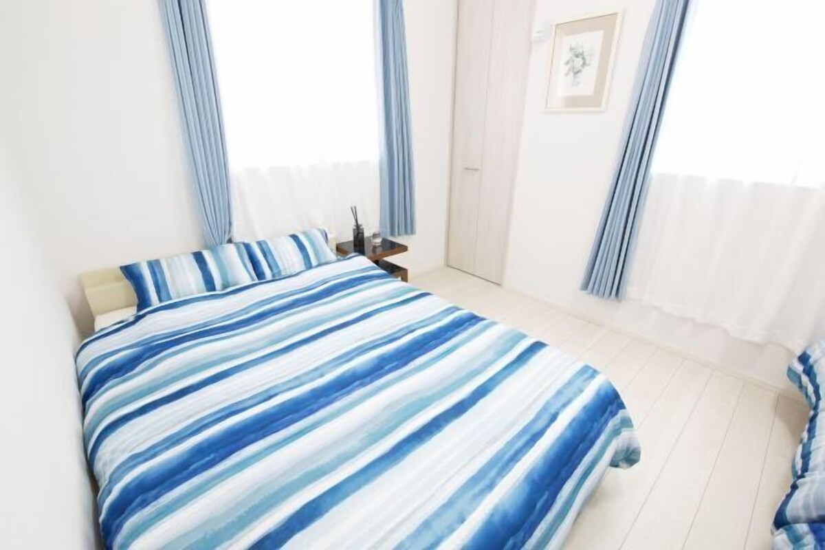 Een slaapkamer met een bed, een nachtkastje, een ingelijst beeld aan de muur en een deur.