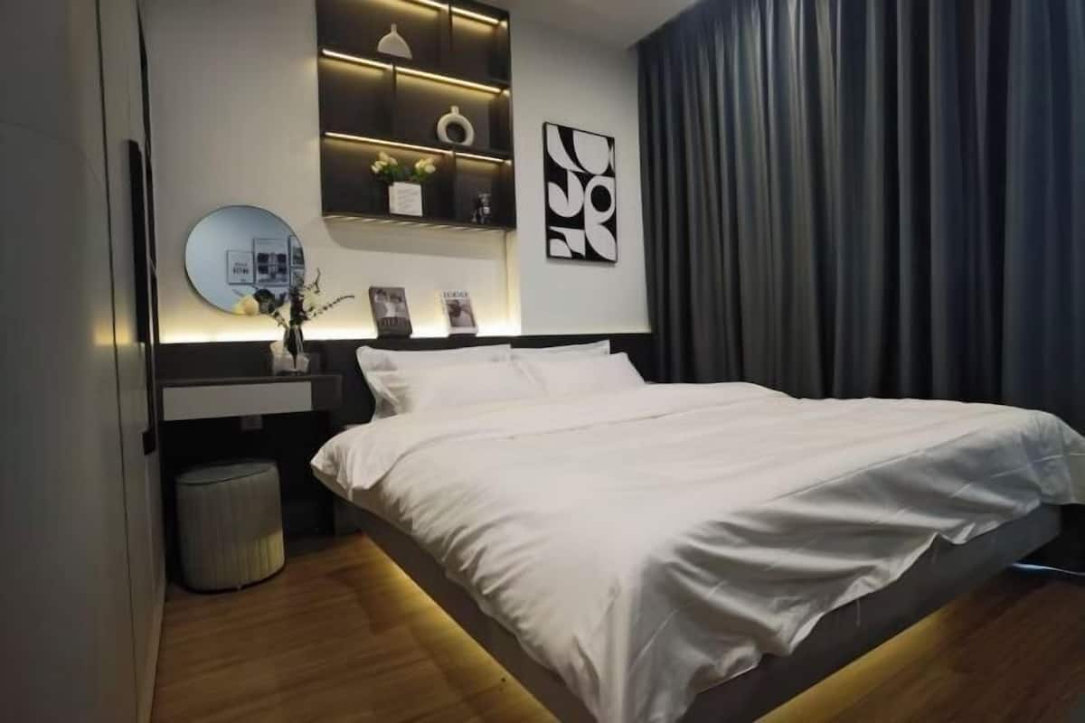 A modern bedroom with a bed, bedside tables, a mirror, and a wall-mounted shelf with decorative items.