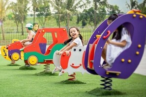 Children playing on colorful, spring-mounted ride-on toys in a grassy area.