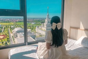 Une chambre dotée d’une grande fenêtre, d’un lit et offrant une vue sur le paysage urbain.