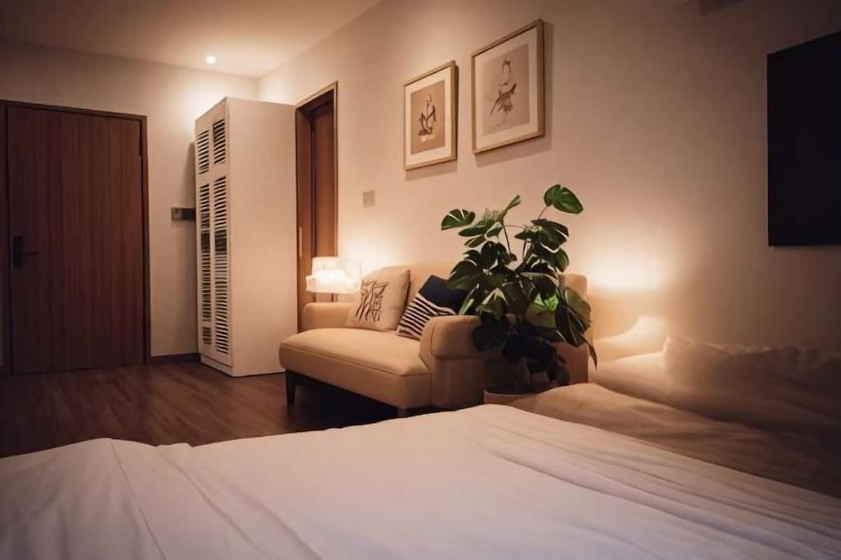 A hotel room with a bed, a sofa, a potted plant, a nightstand with a lamp, and a door.
