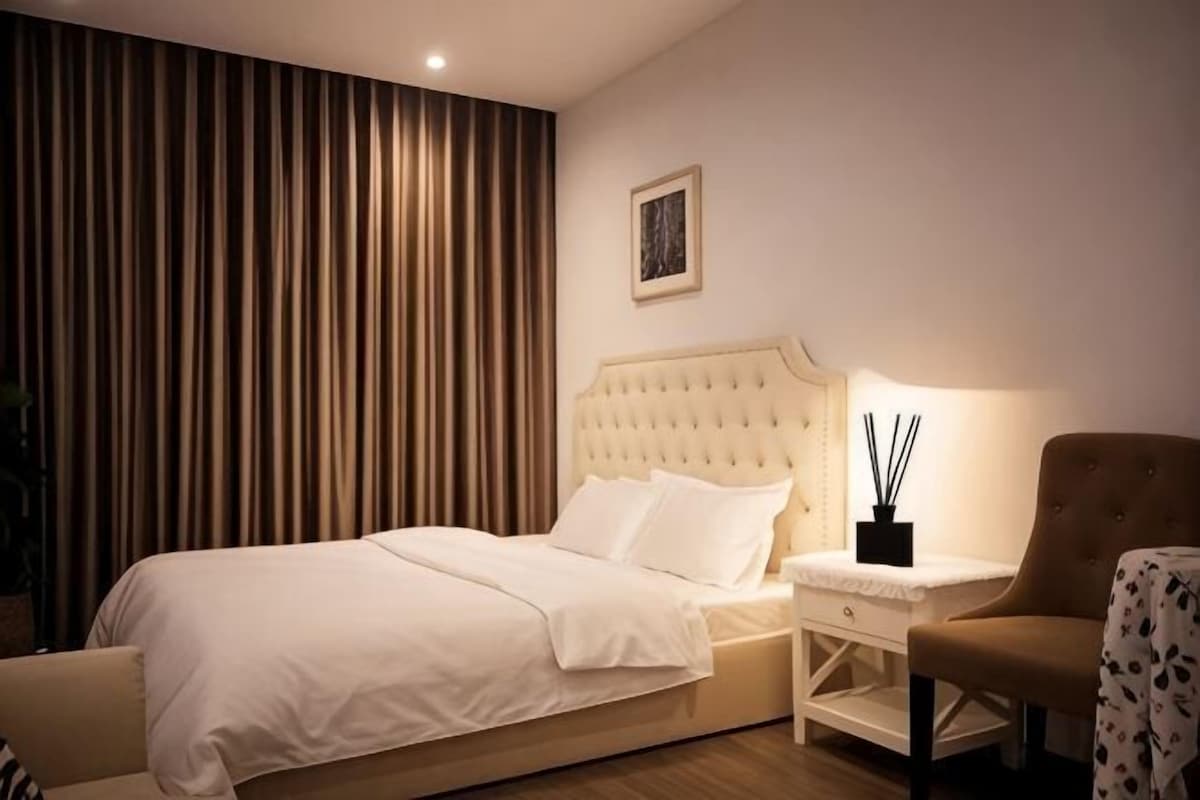A hotel room with a bed, bedside table, chair, and curtains.
