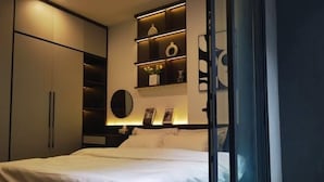 Une chambre à coucher comprenant un lit, des étagères intégrées, un miroir et une porte vitrée donnant sur une autre pièce.