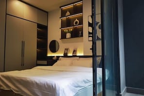 Une chambre à coucher comprenant un lit, des étagères intégrées, un miroir et une porte vitrée donnant sur une autre pièce.