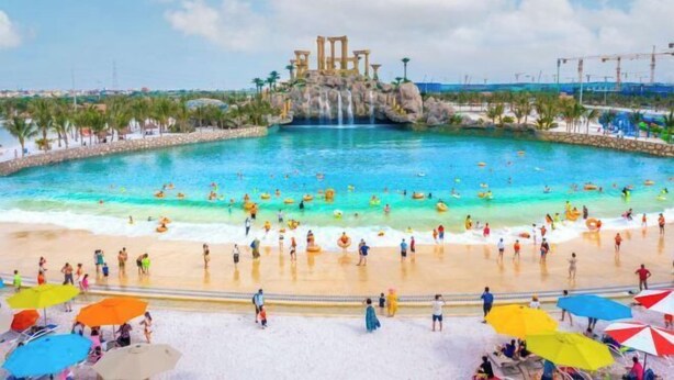 Une piscine avec une cascade, entourée de vacanciers et de parasols.