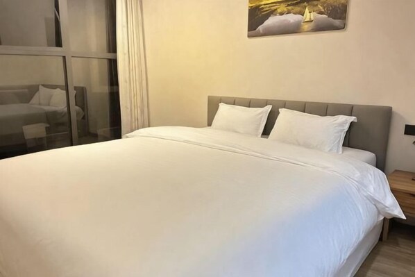 A neatly made bed with white bedding, a grey headboard, and a painting on the wall.