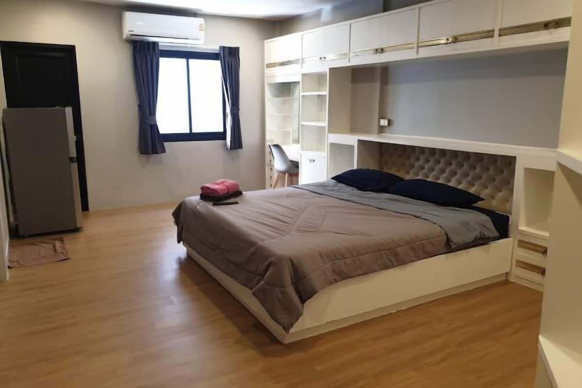 A bedroom with a bed, built-in shelving, a desk, and a refrigerator.