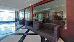 A modern lobby with a glass wall, a seating area, and a check-in counter. - The Loft Hostel by Evernent (Miri)