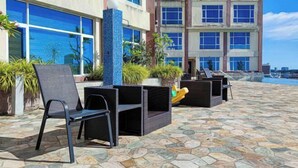 Outdoor seating with chairs and tables, a stone-tiled patio, and a building with large windows and a pool in the background. - The Loft Hostel by Evernent (Miri)