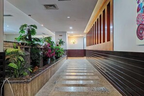 A hotel lobby with a marble staircase, potted plants, and a wall with a decorative pattern.