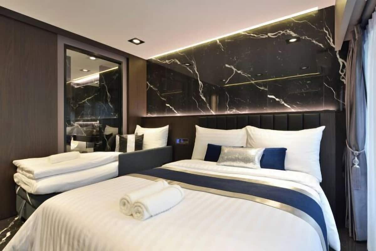 A modern hotel room with a large bed, a dark marble headboard, and a large mirror.