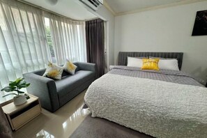 A hotel room with a bed, a grey sofa, a small table with a plant, and a window with curtains. - Cozy Studio on Nimman 8/ Walk to Cafes & Nightlife (Chiang Mai)