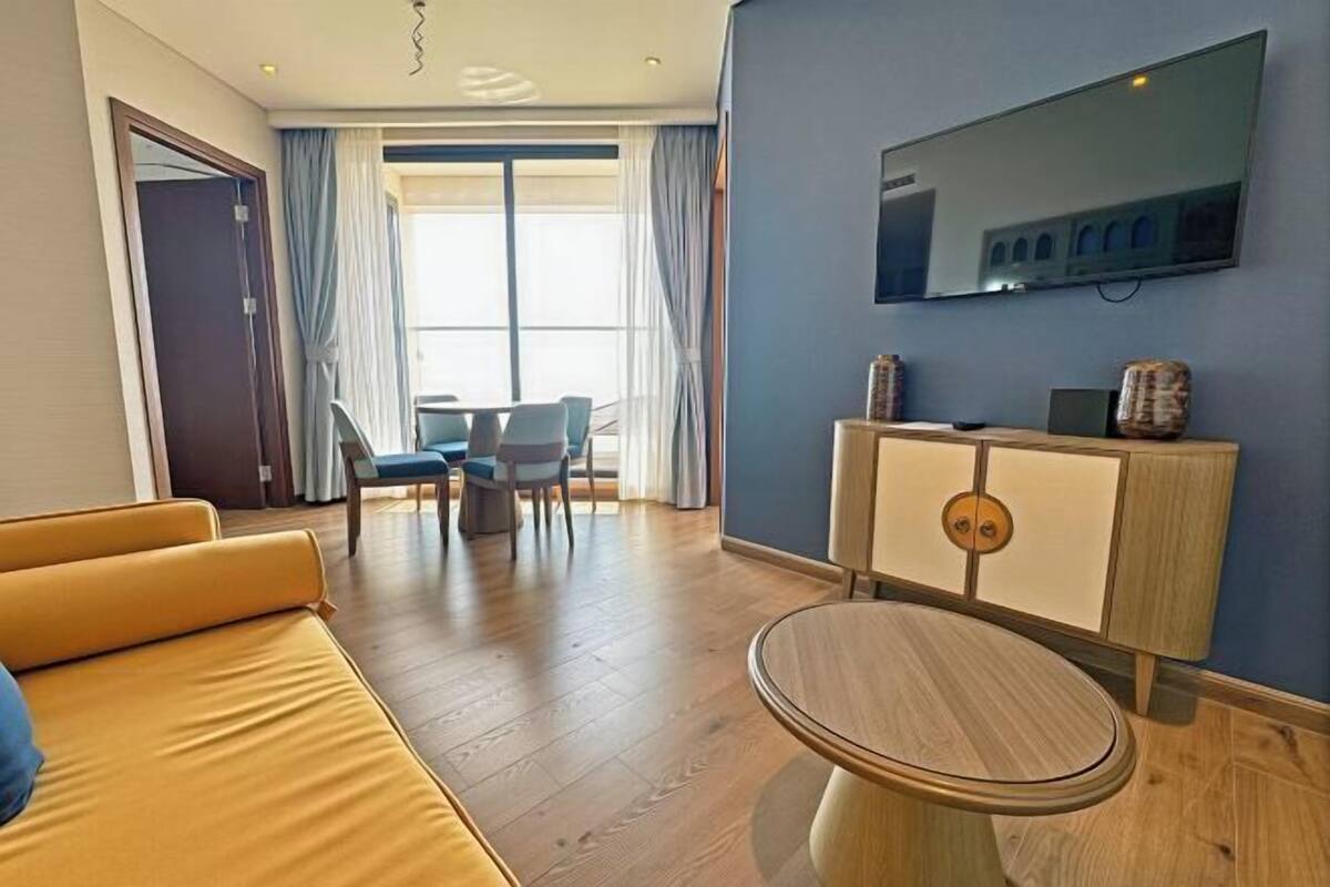 A modern hotel room with a sofa, a round table, a television, and a balcony with curtains.