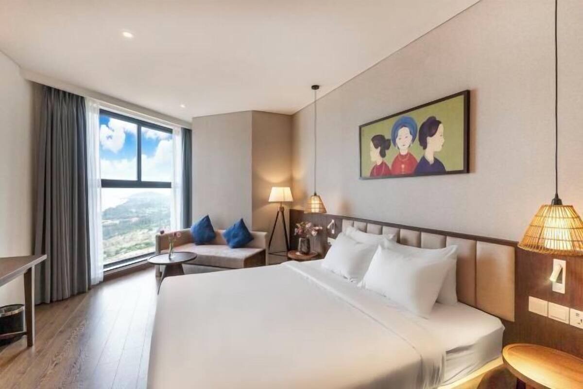 A hotel room with a large bed, a desk, a chair, a small table, and a painting on the wall.
