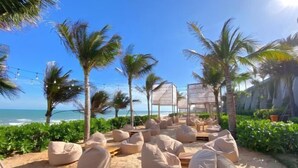 Outdoor seating with bean bags and a wooden table, surrounded by palm trees and a view of the ocean. - Mandala Heaven Dreamscape Hotel & Resort (Phan Thiet)