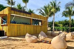 Una casa de playa con fachada de madera, una zona de bar y varios sillones de arena.