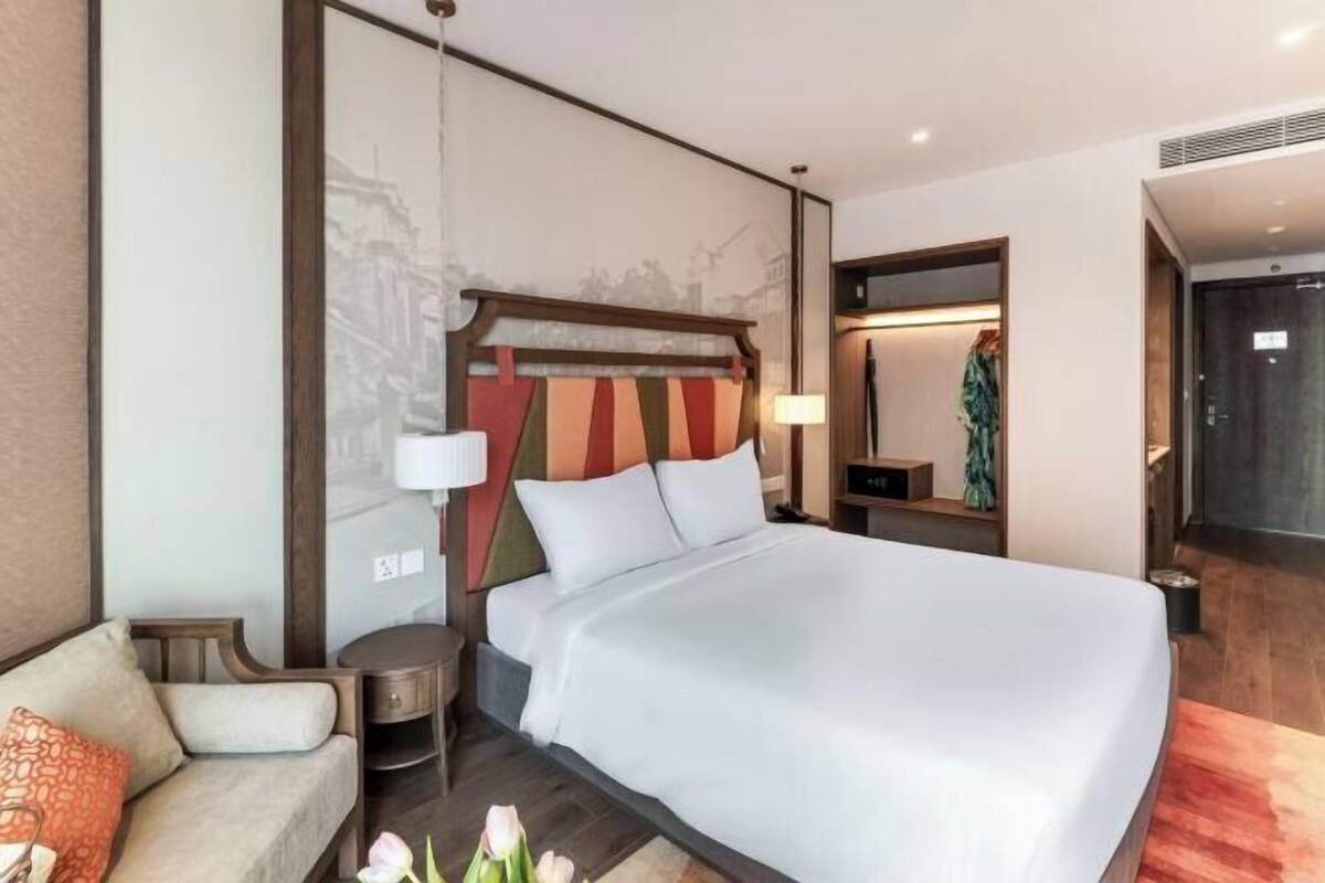 A modern hotel room with a large bed, a sofa, a nightstand, and a mirror.