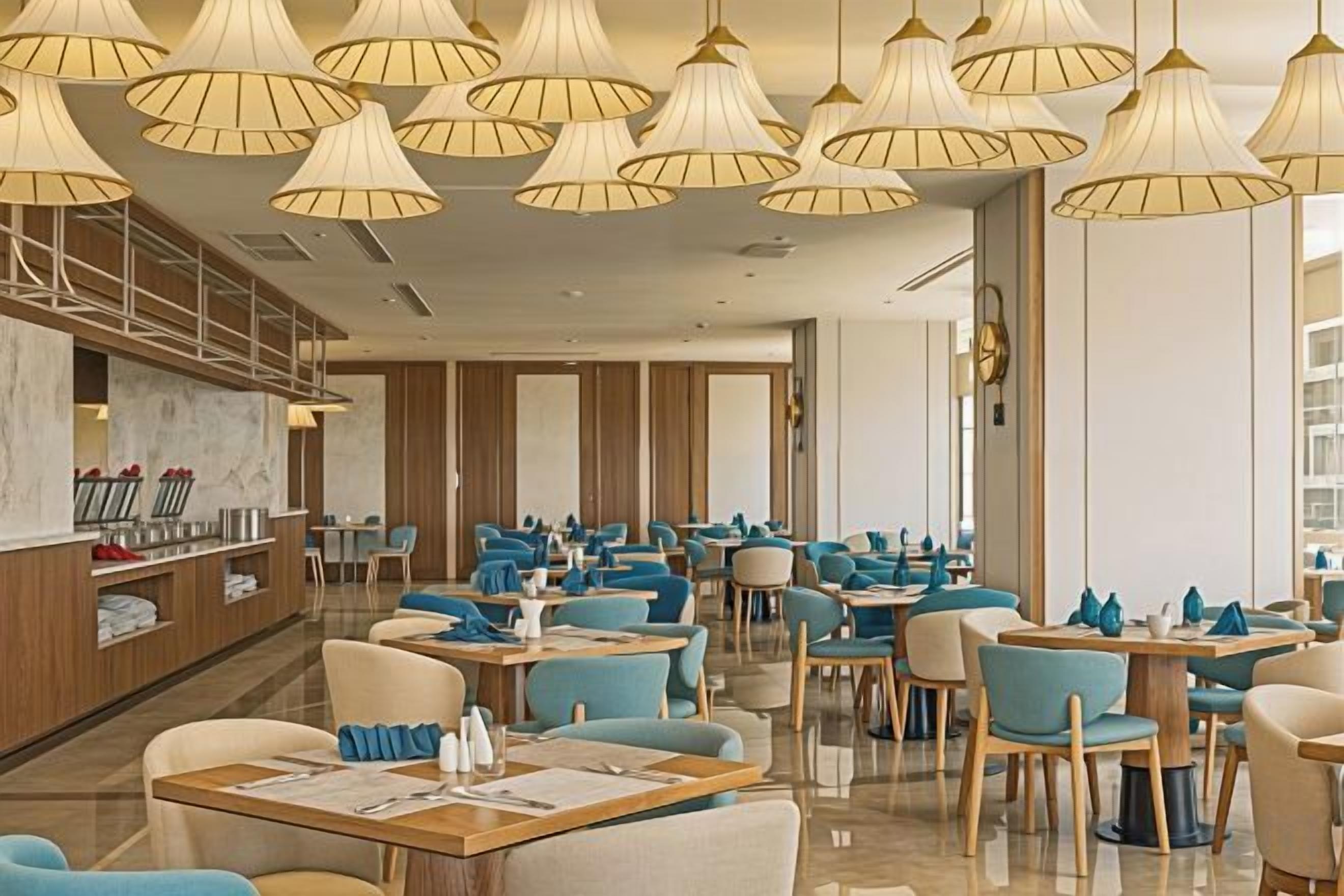 A modern restaurant with multiple dining tables and chairs, a bar area, and pendant lighting.