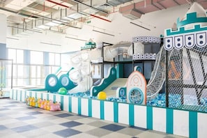 Un espace de jeux intérieur avec un toboggan, un filet d’escalade et une piscine à balles.