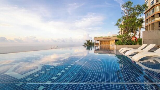 A infinity pool with a clear view of the ocean, lounge chairs, and a building with a sign. - Mandala Heaven Dreamscape Hotel & Resort (Phan Thiet)