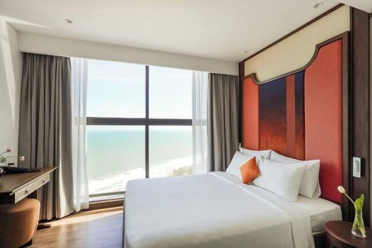 A hotel room with a large bed, a desk, and a view of the ocean.