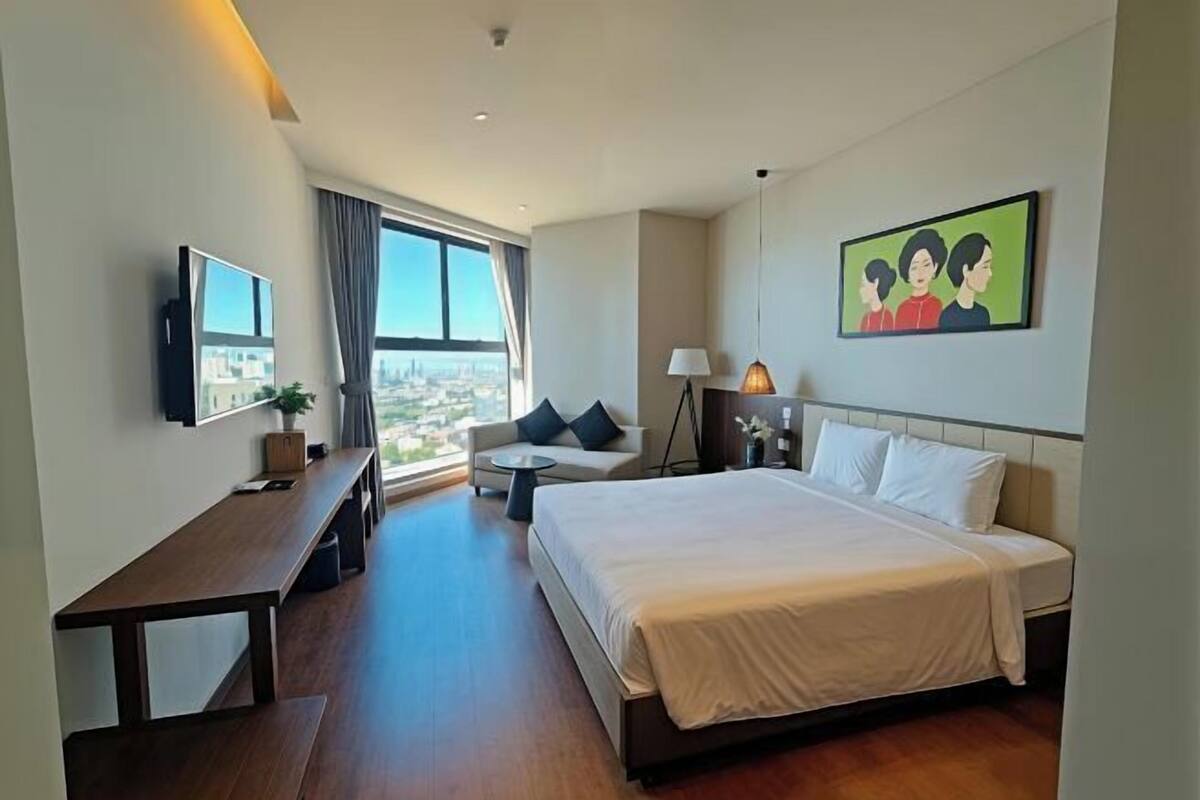 A hotel room with a large bed, a sofa, a desk, and a TV.
