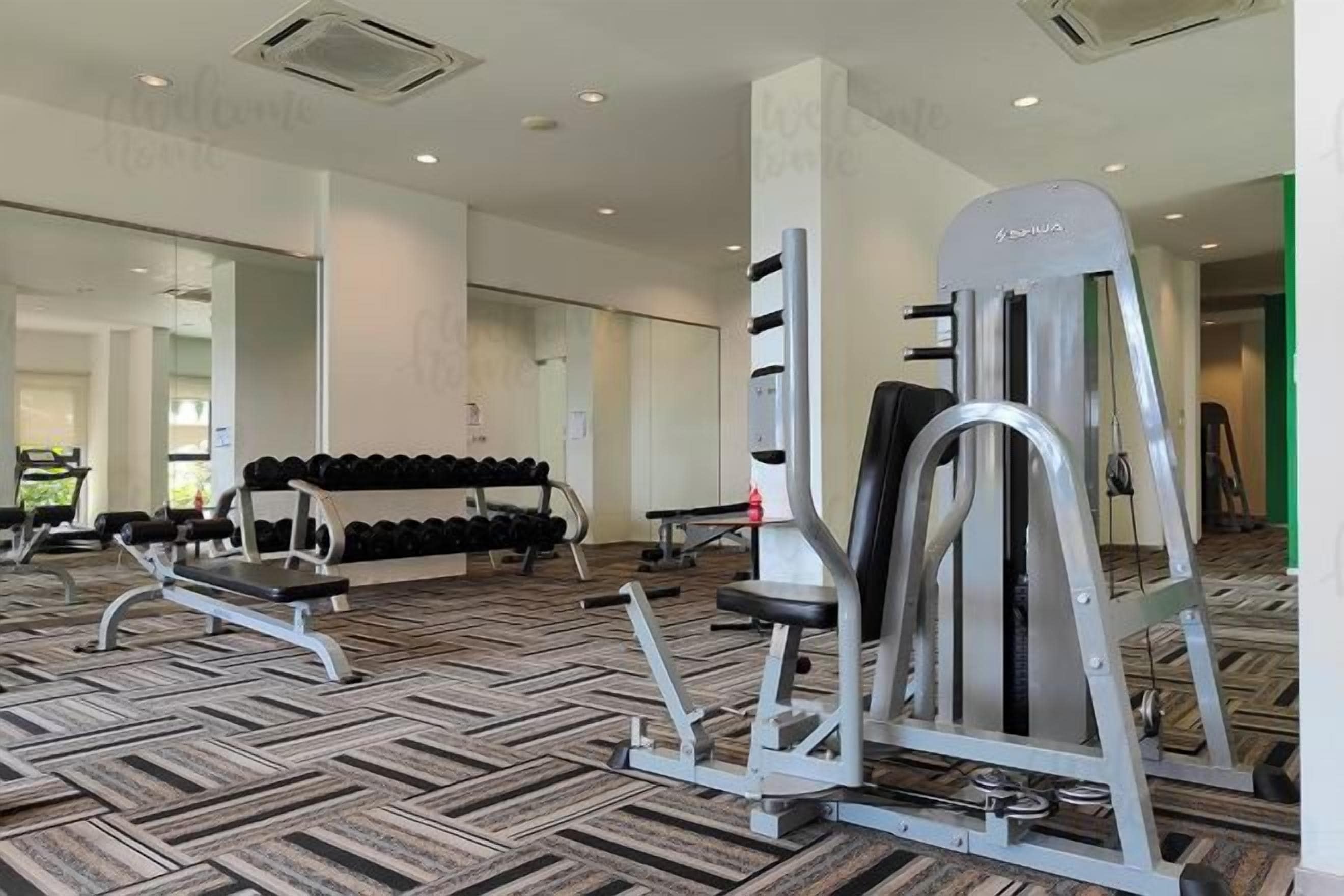 A gym with exercise equipment, a mirrored wall, and a patterned carpet.