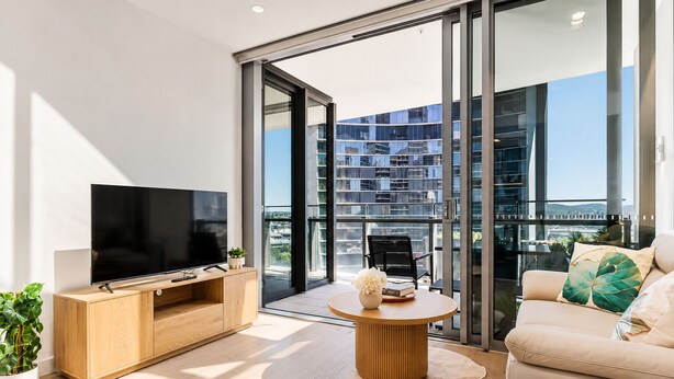 Un soggiorno moderno con una TV a schermo piatto, mobili in legno, un tavolino rotondo e un divano con cuscini decorativi.