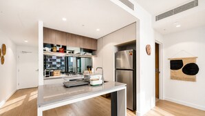Una cucina moderna con frigorifero in acciaio inox, lavastoviglie e forno a incasso. Un pensile in legno sopra il lavello e una dispensa a parete.