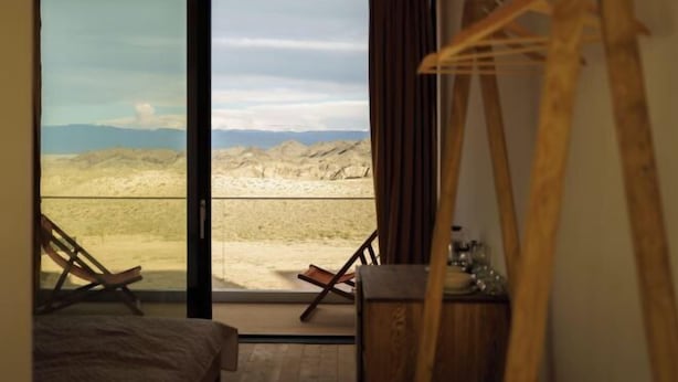 A room with a bed, a chair, a wooden desk, and a large window with a view of a desert landscape. - Pana Unique Charyn (Enbekshikazakh District)
