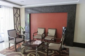 A hotel lobby with a seating area, a table with papers, a potted plant, and a decorative wall. - Sarasota Genlex Condominium (Pasay)