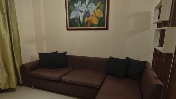 En brun sofa med sorte puder, et blomsterbillede på væggen og et hvidt reolsystem.