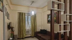 A living room with a sofa, a ceiling light, a window with curtains, and a wall-mounted shelf. - Sarasota Genlex Condominium (Pasay)