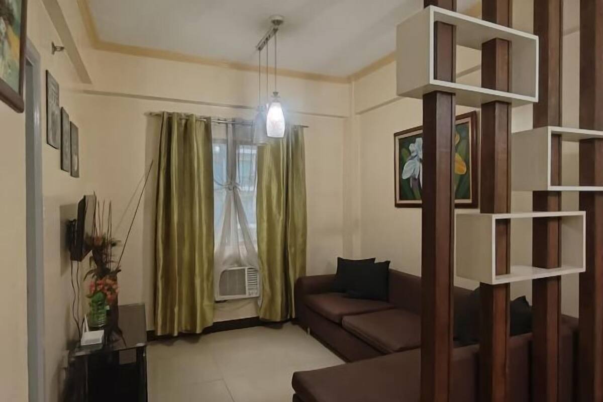 A living room with a sofa, a ceiling light, a window with curtains, and a wall-mounted shelf.