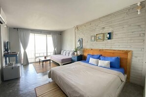 Un dormitorio con cama, escritorio, sofá, ventana con cortinas y pared de ladrillo.