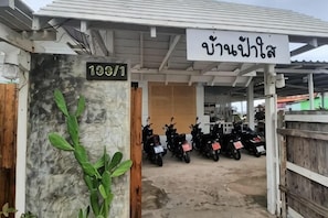 Un espace de stationnement couvert où sont garées des motos, un panneau avec du texte et une plante.