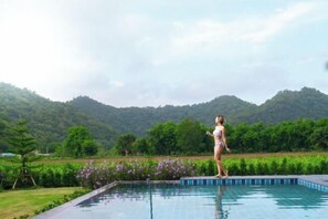 Une personne se tient près d’une piscine, avec une vue sur des collines verdoyantes.