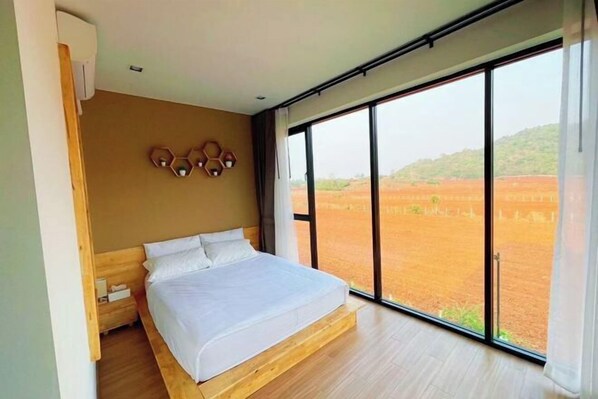 Une chambre avec un grand lit, une tête de lit en bois, une table de chevet et une vue sur un paysage rouge par de grandes fenêtres.