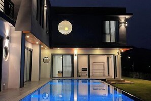 A modern two-story house with a swimming pool, a circular skylight, and a well-lit exterior.