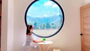 Een kamer met een rond raam, een kleine tafel en iemand die bij het raam zit.