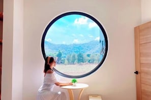 A room with a round window, a small table, and a person sitting by the window.