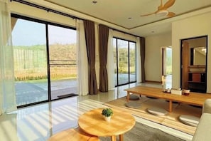 A spacious room with large sliding glass doors, a wooden dining table, a small round table with a plant, and a sofa.