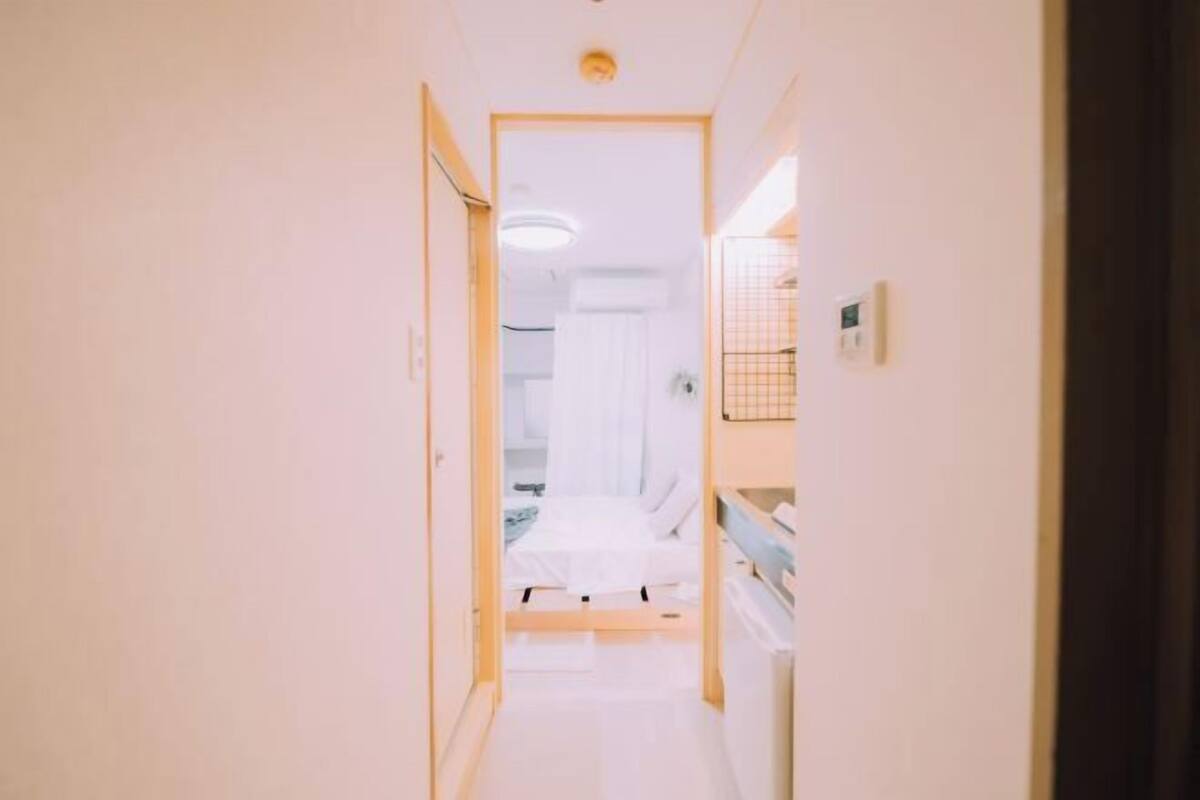 A narrow hallway leading to a bedroom with a bed and a nightstand.