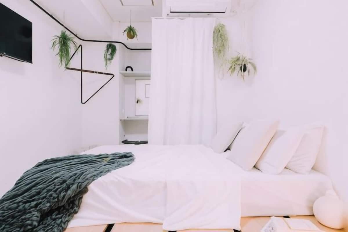 A bedroom with a bed, white walls, a white curtain, and a white sofa.