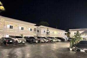 A hotel parking lot with multiple cars, a building with balconies, and a well-lit entrance. - Duangdeerojehouse (Chon Buri)